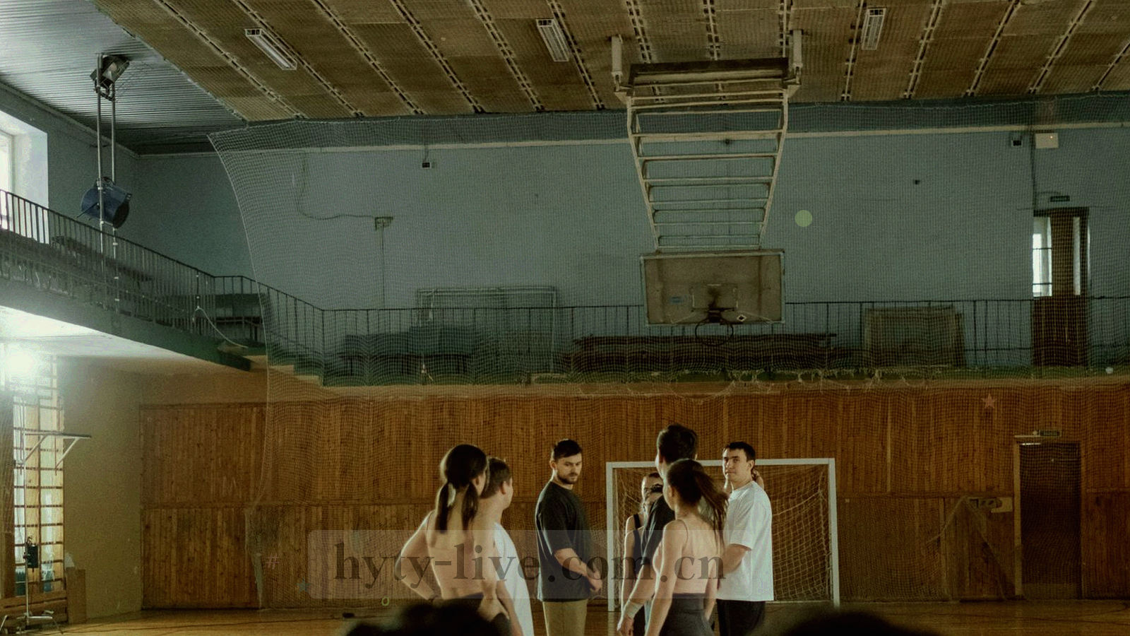 夜色中的球场俯拍，顶灯照亮草皮，看台上是一片紫青色的观众剪影